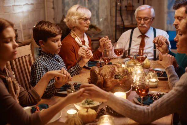 istock Small boy and his extended family holding hands while praying before Thanksgiving dinner at dining table. 1436773075