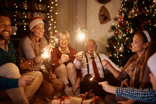 Happy multi-generation family using sparkles and having fun while celebrating Christmas at home. Cheerful extended family having fun with sparklers while celebrating Christmas together at home. family christmas party stock pictures, royalty-free photos & images