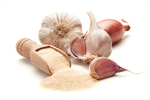 Ground dried garlic on a wooden spatula surrounded by whole heads of garlic