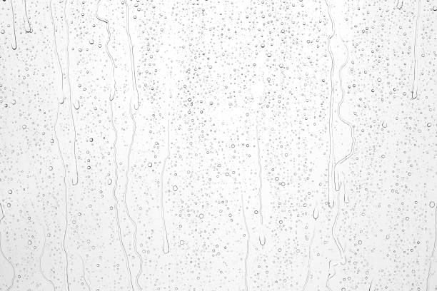 Drops of rain on glass against blue sky and white clouds.