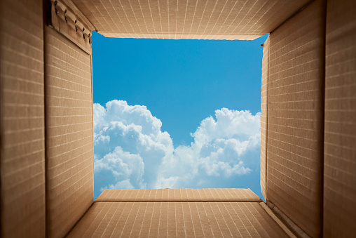 Looking though cardboard open box toward blue sky background.