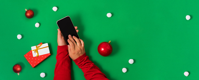 Girl touches smartphone screen with fingers, online payment for Christmas shopping, green background, flat lay. Online shopping concept. Only hands in the frame