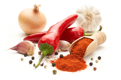 Hot red pepper ground on a wooden spatula on a white background. Whole hot peppers