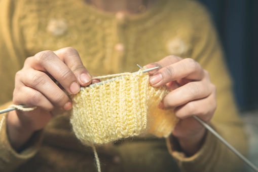 Close-up video of a woman hands knitting a wool sweater at home in winter.