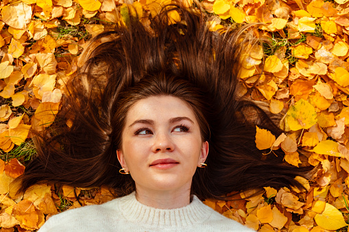 Beautiful woman laying on yellow autumn leaves looking up in the sky