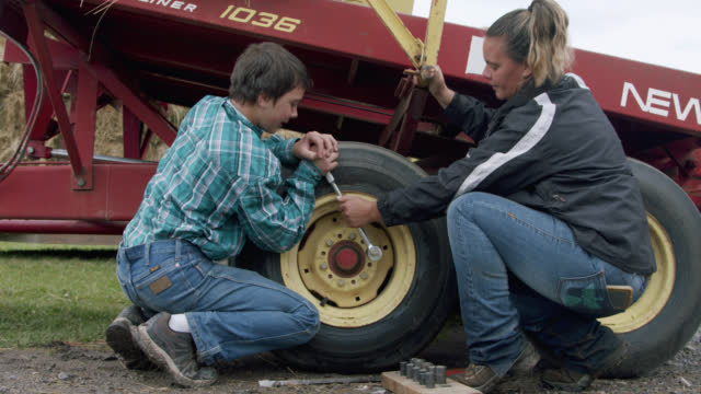 Middle-Aged Caucasian Mother Teaching and Helping Her Young Teenage Son How to Change a Tire on a Bale Wagon for Accumulating, Stacking, and Moving Hay or Straw on a Small Town Family-Owned Ranch in Colorado, USA