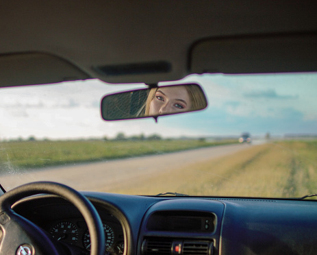 A beautiful girl looks in the car mirror/ inside a car / cinematic photo