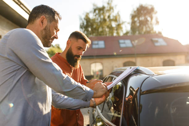 Salesman giving his customer a clipboard to sign after selling him a car stock photo