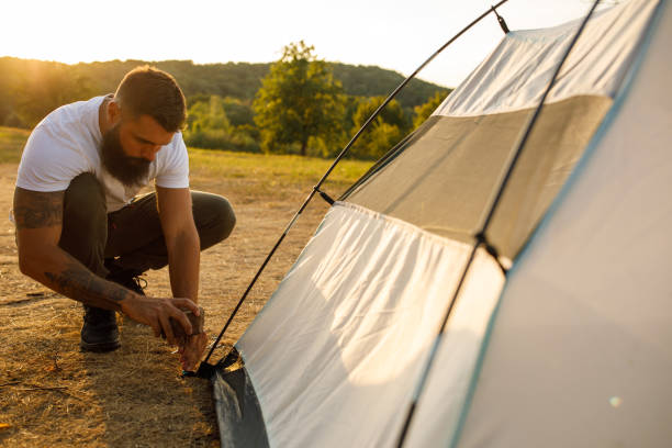 istock Young man hammering a tent peg into the ground using a rock 1436783843