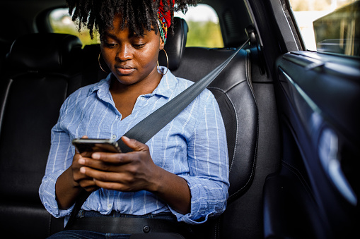 Copy space shot of young Black woman riding in the back seat of a taxi and texting a friend via smart phone.