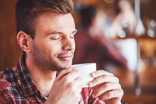 Portrait of handsome young man holding a cup and enjoying coffee while sitting in a modern urban cafe