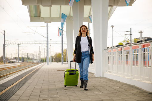 Front view of mid adult businesswoman going on a business trip. She is walking on the platform at the train station, dragging her suitcase.