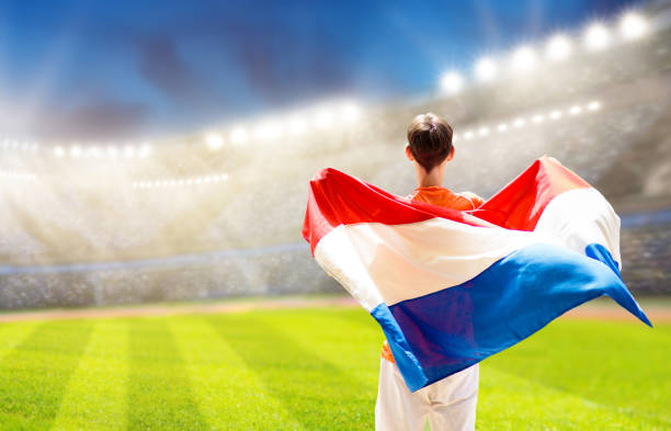 Netherlands football supporter on stadium. Dutch fans on soccer pitch watching team play. Player or fan with flag and national jersey cheering for Holland. Championship game. Hup Holland
