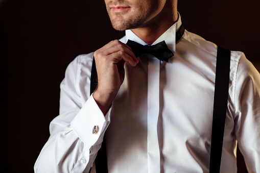 Man the groom in a wedding formal costume with butterfly. Suit, Hands, care, tie, to correct, to adjust, fashion, bow. Handsome business man in a suit. Portrait of sexy man.