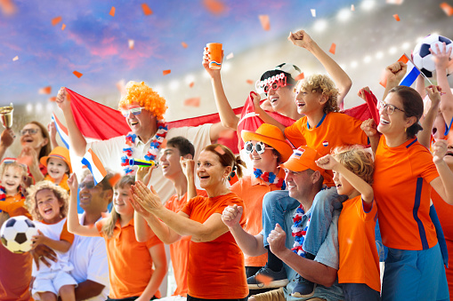 Netherlands football supporter on stadium. Dutch fans on soccer pitch watching team play. Group of supporters with flag and national jersey cheering for Holland. Championship game. Hup Holland