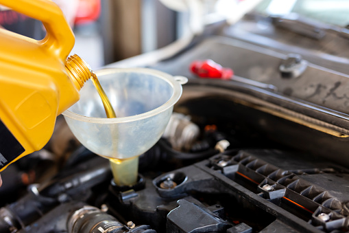 Pouring motor oil for motor vehicles from a gray bottle into the engine