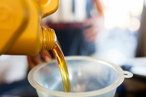 Pouring motor oil for motor vehicles from a gray bottle into the engine