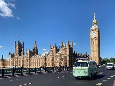 Old VW kombi campervan (1974) driving in front of the Houses of Parliament and Big Ben in London early morning in summer.