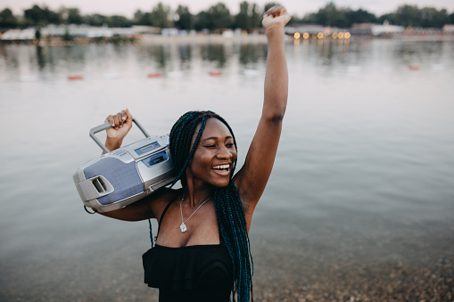 A portrait of a young African-American woman enjoying time at the river bank while listening to an old boom box.