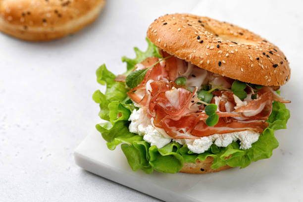 istock Sandwich with prosciutto, cream cheese and microgreens, bagel with ham, lettuce for breakfast on marble board. Space for text, close up. 1436800444