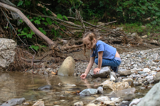 a little girl during a family hike in the mountains collects water from a mountain river in her palm