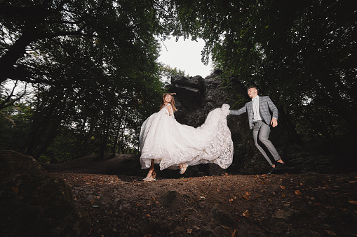 Wedding couple are walking in the forest. bride in long white dress and groom in suit.