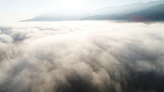 Aerial view of clouds and landscape under them. Shot. Top view of the clouds under the sky. Under the clouds shot from a bird's flight, the sun shines on the clouds.
