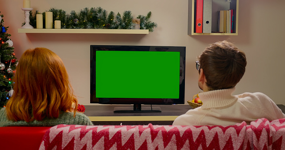 Family Couple Watching Green Screen TV Mockup Sitting on Couch in Living Room Together. Rear View on Casual People who Watching TV Green Screen. TV Show or News in Home Rest