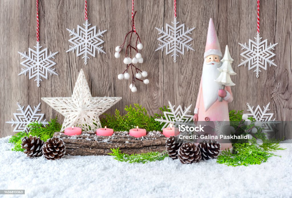 Advent candles, Santa Claus and a Christmas star in the snow. Advent candles, Santa Claus and a star in the snow are decorated with spruce branches. Christmas and New Year decor. Grey wooden background. Candlestick Holder Stock Photo