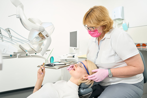Patient looks in the mirror while the dentist waits while sitting on a chair