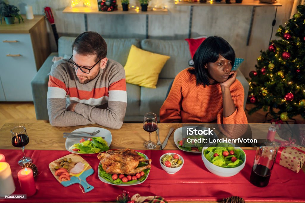 Couple ignoring each other after an argument Young unhappy multi ethnic couple ignoring each other after an argument during Christmas dinner Christmas Stock Photo