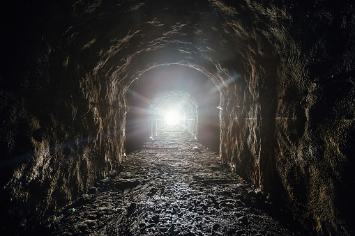Dark underground tunnel. Light at the end of tunnel.
