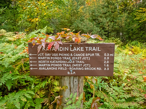 Katahdin Lake Trail sign includes nearby hiking trails and distances in early fall from Lake Katahdin, Maine, in early fall