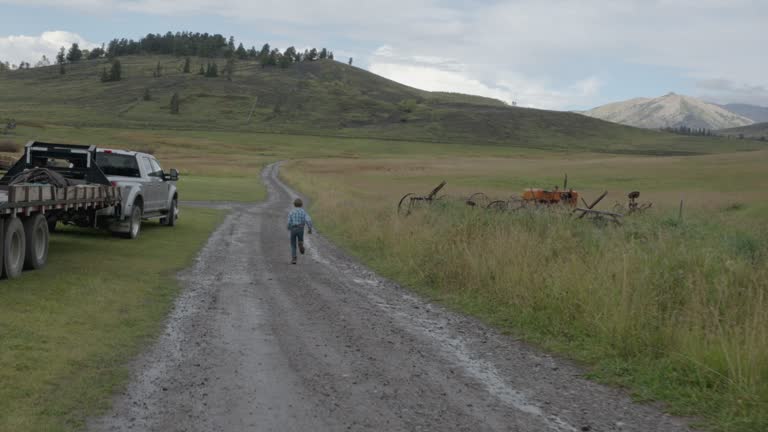 Young White Farm Boy Running Down a Dirt Road Driveway In Front of His Homestead in the Rocky Mountains of Southwestern Colorado Near Telluride