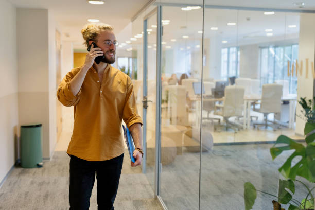 istock Young businessman using smart phone while walking in the office corridor 1436830296