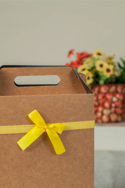 istock Gift wrapping with a yellow bow and flowers in the background. 1436830313