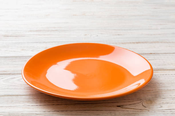 istock Perspective view of empty orange plate on wooden background. Empty space for your design 1436834349