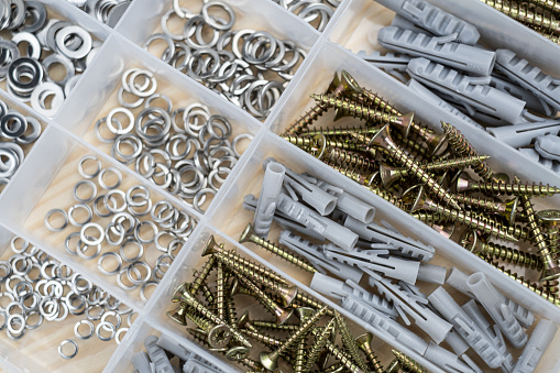 Screws and dowels of various sizes in A transparent plastic box container Organized, on a wood bg. Close up, top view.