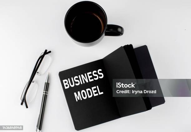 Business Model Written Text In Small Black Notebook With Coffee Pen And Glasess On A White Background Blackwhite Style Stock Photo - Download Image Now