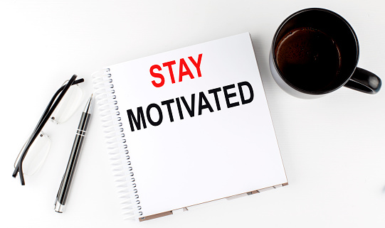 Coffee,glasses,pen and notebook written with STAY MOTIVATED , on a white background.