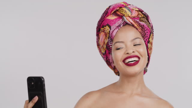 Beauty, phone selfie and black woman in turban or African head scarf on gray studio background. Fashion, makeup and Nigerian skincare model on 5g mobile for social media, picture or photo post on web