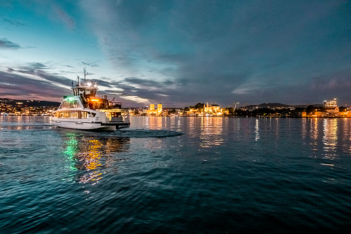 Electrical battery operated ferry at Oslo Fjord at night with illuminated citiy skyline in the back , 4k resolution