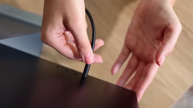 Person hand connects black USB-C or Type C power cable to computer or monitor
