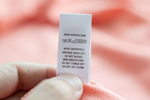 Hand hold and reading at white laundry care washing instructions clothes label on pink shirt