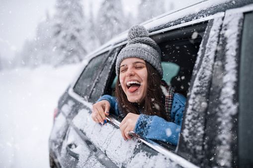 Young woman sticking her tongue out to taste the snow flakes throuhg the car window.