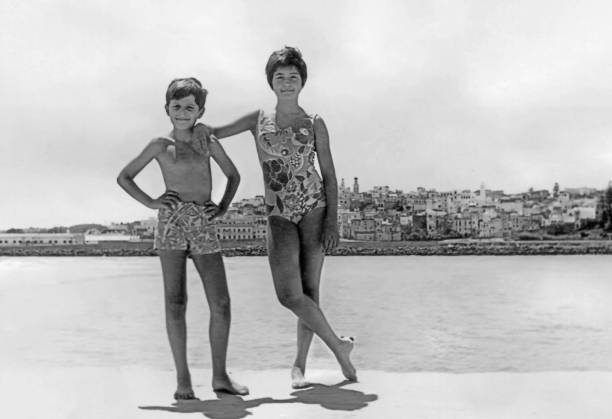 Vintage image from the sixties, a boy and a girl posing together smiling at the beach, in Larache (Morocco) Vintage image from the sixties, a boy and a girl posing together smiling at the beach, in Larache (Morocco) male swimsuit standing arm around stock pictures, royalty-free photos & images