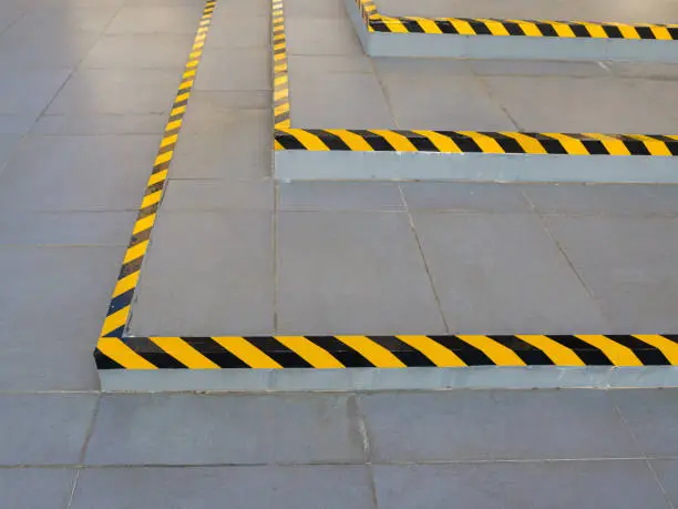 Photo of Black and yellow hazard warning safety stripe tape stuck on the stairs. Caution strip line on the edge of different level floor.