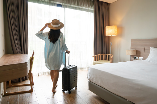 Joven viajera asiática con equipaje y sombrero de paja en la habitación del hotel después del check-in. Concepto de viaje y vacaciones de verano. Espacio de copia photo