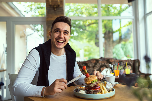 One man young adult caucasian male sitting at the table at restaurant with burgher and french fires potato chips eat alone in day real people copy space happy smile