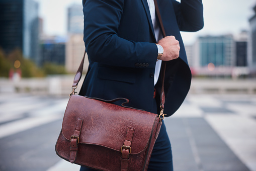 Close-up of a businessman carrying a leather satchel walking outside in the city after work